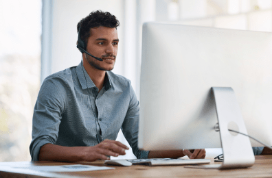 Mann am Schreibtisch mit Headset mit Blick auf einen großen Monitor