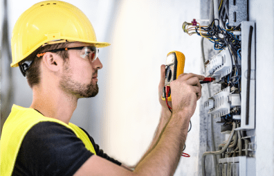 Elektriker mit gelbem Schutzhelm und Schutzbrille überprüft ein Elektroschaltpanel