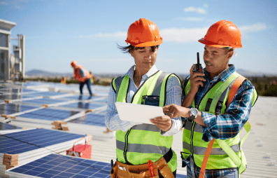 Ein Mann und eine Frau in Schutzkleidung bei der Arbeit auf einem Flachdach mit Solarpanelen