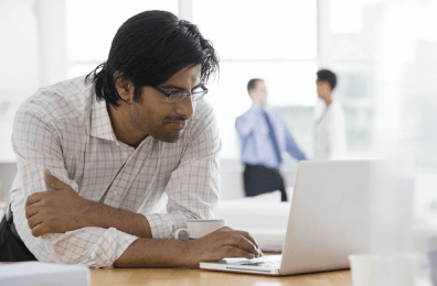 Mann im Hemd bedient im Büro einen Laptop - im Hintergrund Mitarbeitende im Gespräch