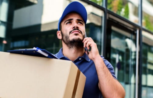 Paketzusteller mit Paket vor Lagerregalen