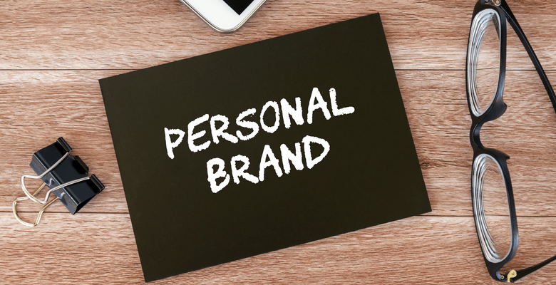 Karte mit dem Text "Personal Brand", Brille und Papierklipp auf einer Tischplatte