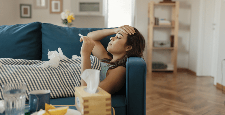 Eine Frau liegt auf der Couch, Augen zu und legt die Hand auf die Stirn.