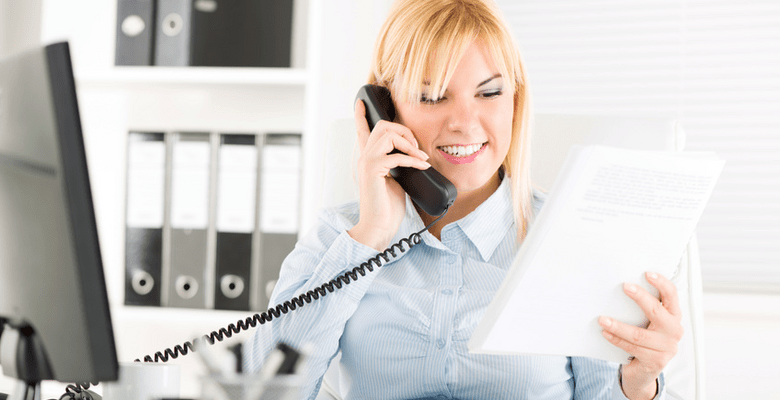 In einem Büro telefoniert eine Frau mit Blick auf Dokumente in der anderen Hand