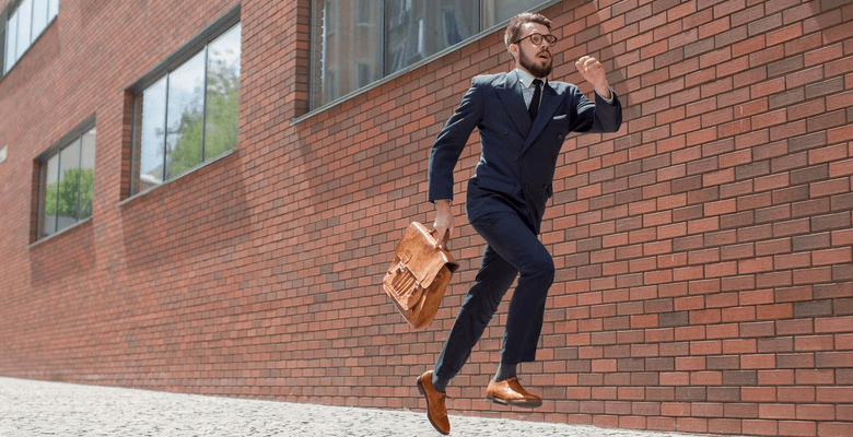 Mann im Business Look und Aktentasche, springend vor einer Backstein-Hauswand