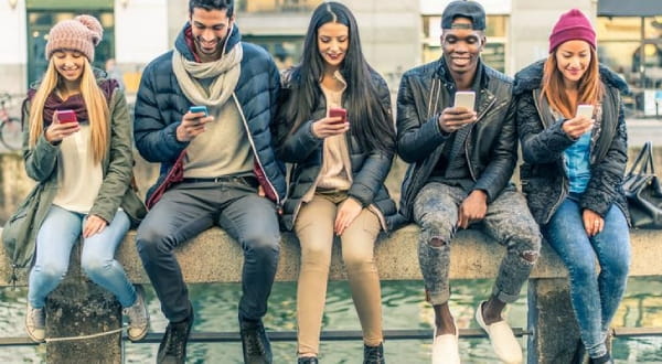 Gruppe junger Menschen auf einer Mauer sitzend und ins Handy blickend