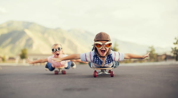 Zwei Kinder, liegend und lachend auf Skateboards unterwegs
