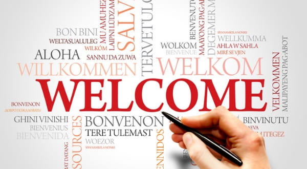 Grafik: "WELCOME" umgeben von "Willkommen" auf mehreren Sprachen und Hand die Stift hält