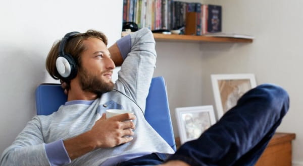Mann mit Kopfhörern auf, Tasse in der Hand, entspannt auf Sessel