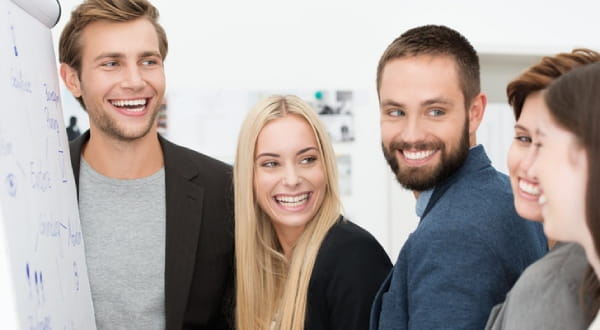 Gruppe vor Flipchart lächelt, alle Blicke auf Frau ganz rechts