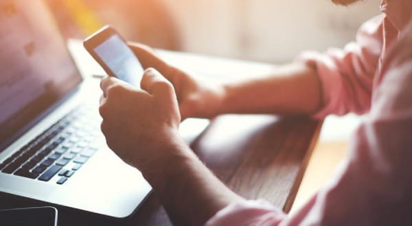 Nahaufnahme, über Tisch mit Laptop bedient Person Handy mit zwei Händen