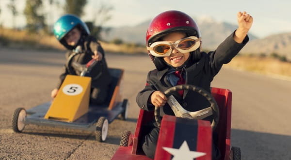 zwei Kinder lachend in Spielzeug-Rennwagen am fahren