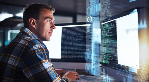 Mann sitzt konzentriert vor PC Screens mit codierten Daten