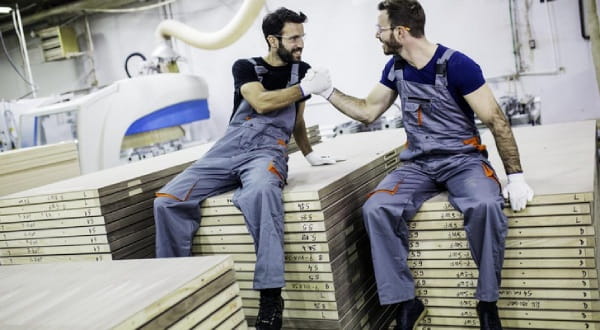 Zwei Männer in Arbeitsklamotten sitzen und geben sich lachend einen Handschlag