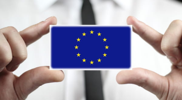 EU-Flagge auf Karte wird mit Fingern im Vordergrund von Anzugträger gehalten