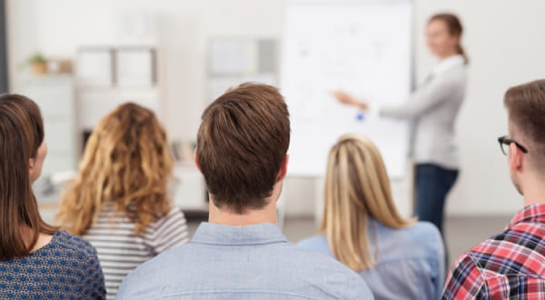 sitzende Gruppe schaut zu Frau an Flipchart