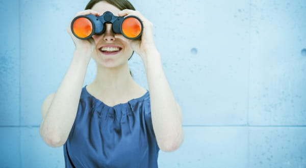 Frau schaut lächelnd durch Fernglas