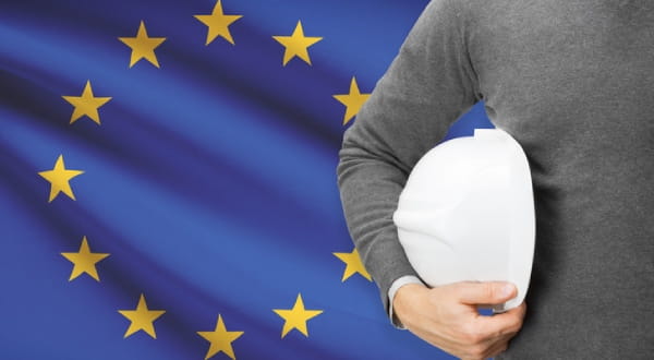 Hintergrund: EU-Flagge; Vordergrund: Person hält Arbeitshelm
