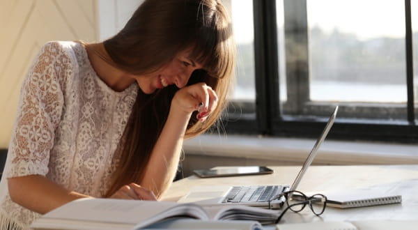 Frau sitzt lachend vor Laptop und Büchern 