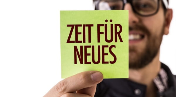 Mann hält Zettel mit "ZEIT FÜR NEUES" in die Kamera