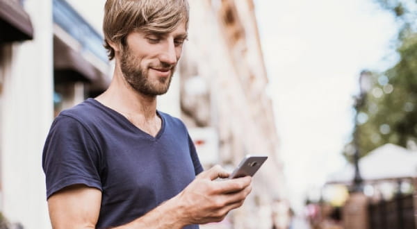 Mann draußen, schaut lächelnd auf Handy
