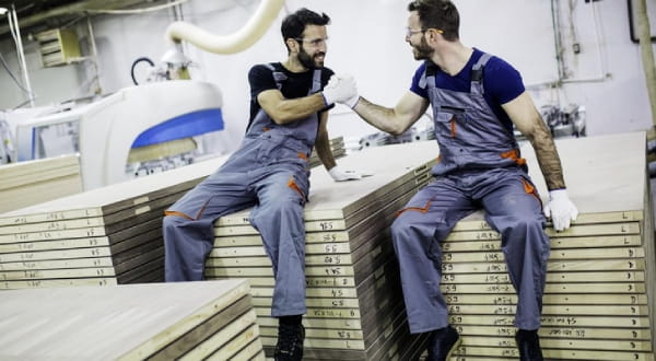 Zwei Männer in Arbeitskleidung sitzen und geben sich einen Handschlag