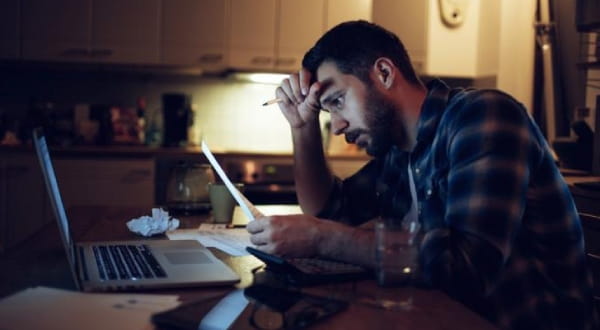Mann sitzt zuhause vor Laptop am Tisch und schaut sich Unterlagen an