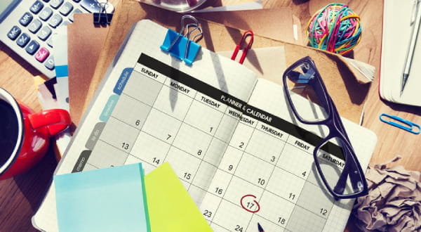 Voller Schreibtisch mit Kaffeetasse, Kalender, Taschenrechner, Notizzetteln, Lesebrille,....