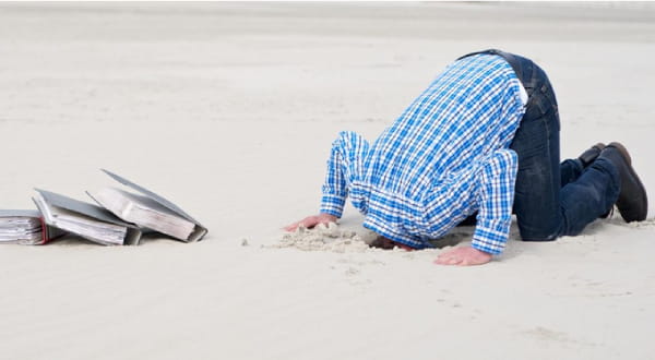 Person steckt Kopf in Sand neben 3 vollen Papierordnern
