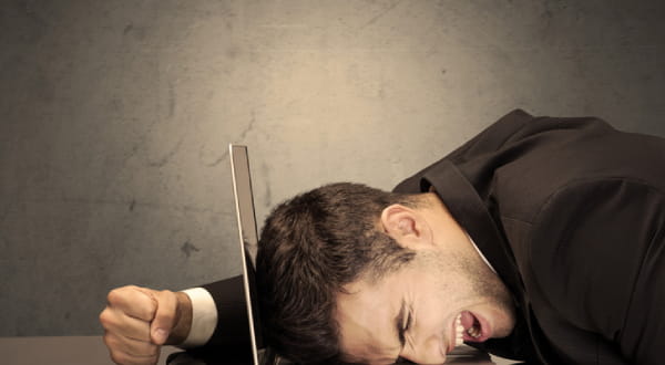 Mann sitzt mit geballter Faust am Tisch, Kopf auf der Laptoptastatur, am schreien